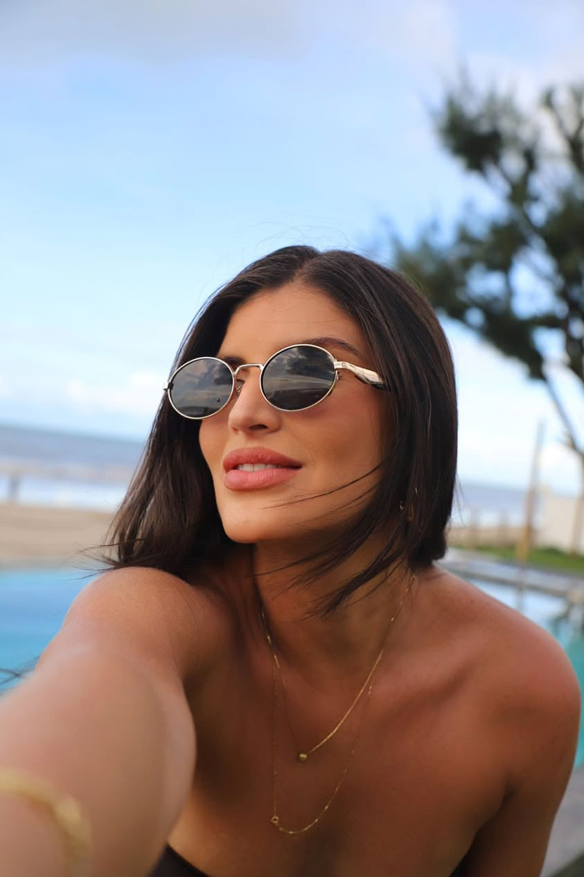 Mulher usando óculos de sol Lana preto com lentes escuras da marca Bjoy em ambiente externo.